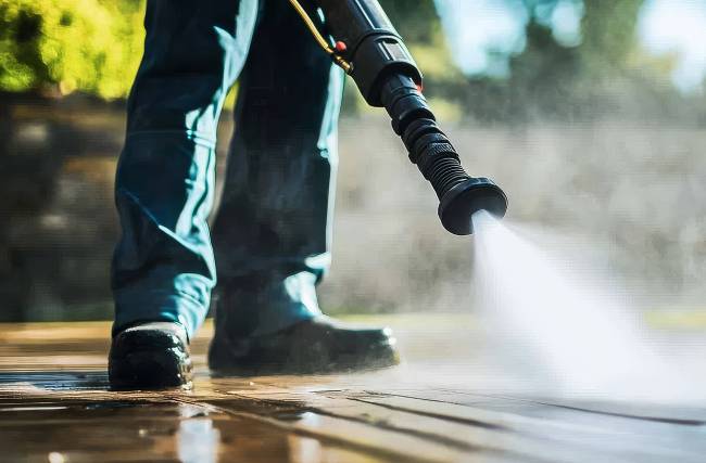 Person som spolar med en högtryckstvätt på en trall. 